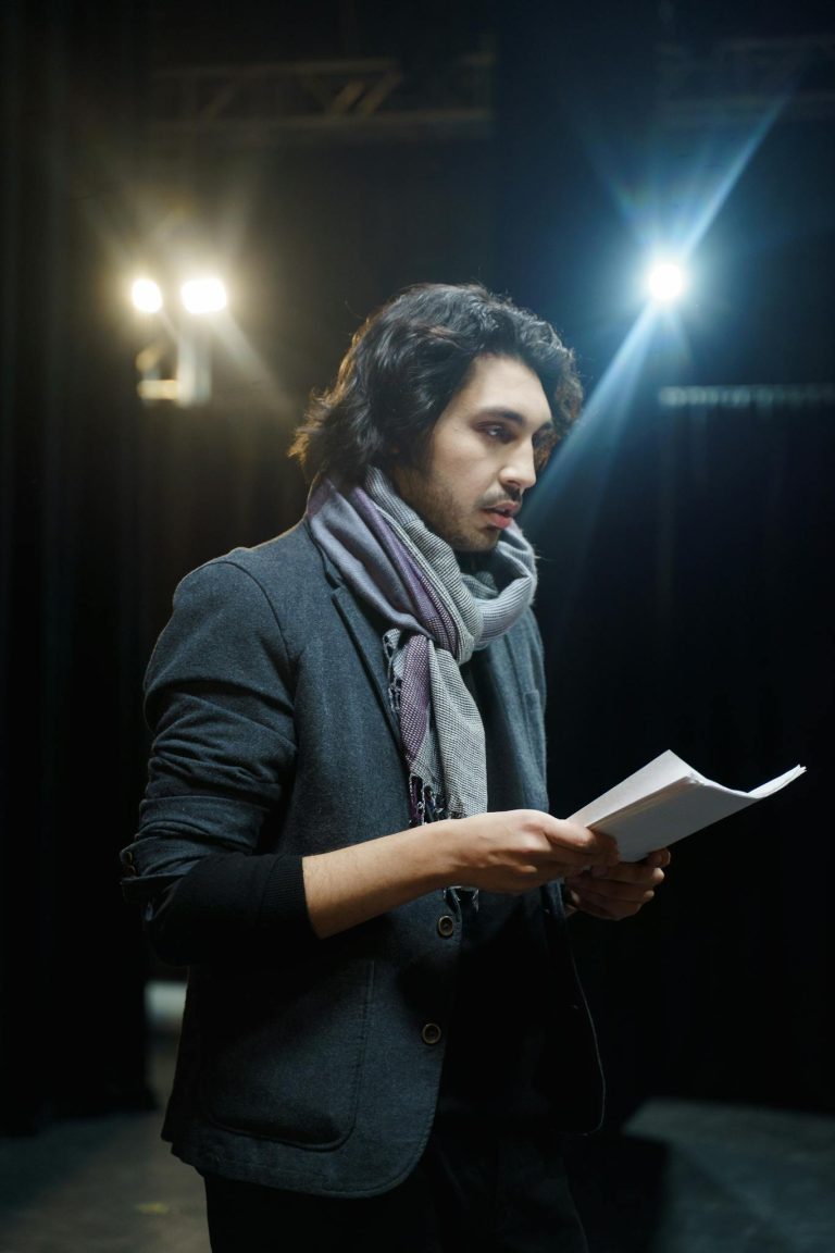 Actor rehearsing a script on stage under bright spotlights.
